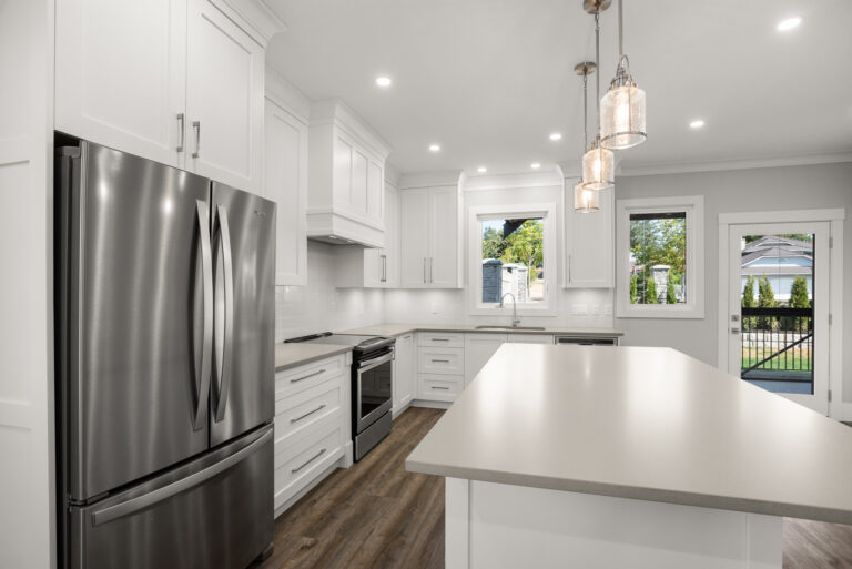 Bright white kitchen with a stainless steel French-door refrigerator, white cabinets, and a large island under pendant lights.