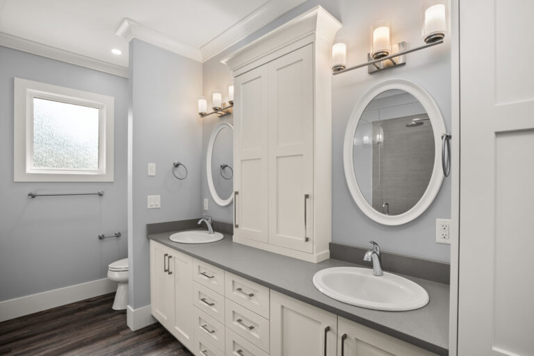 Modern bathroom with a double vanity, two oval mirrors, and wall-mounted light fixtures on gray walls.